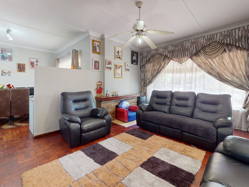 A living room featuring parquet flooring, a ceiling fan, and a brick fireplace, offering a comfortable and traditional living space.