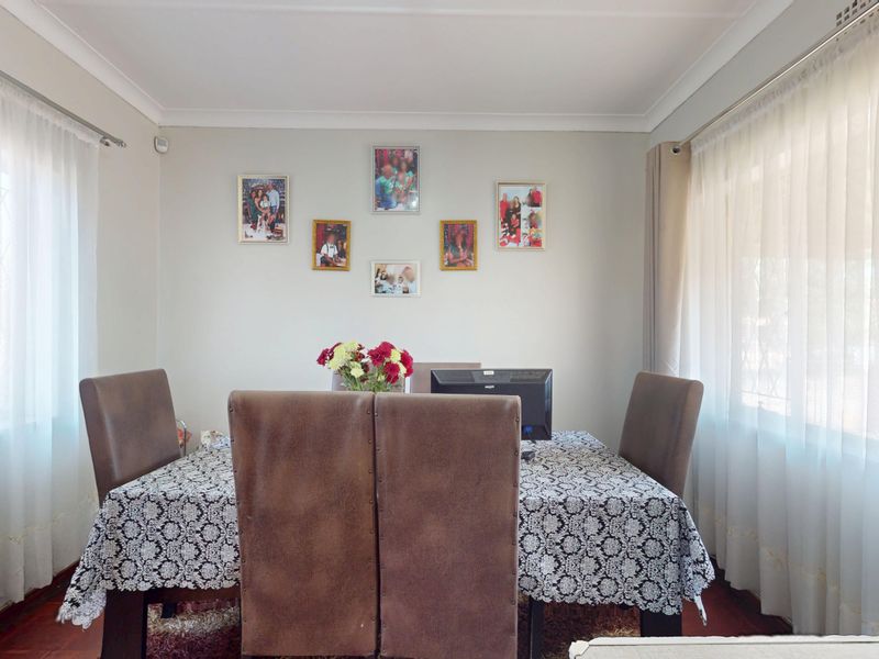 A well-lit dining room featuring neutral walls, cove cornicing, and dual window treatments, providing a functional space for family meals.