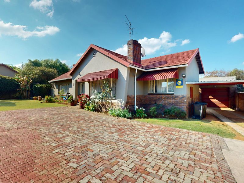 Front view of a single-story house featuring a brick paved driveway, tiled roof, brick chimney, and an attached carport.