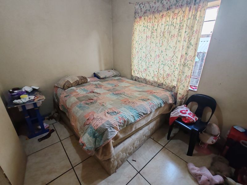 A bedroom featuring tiled flooring and a window with curtains, requiring cosmetic updates to the wall finishes.