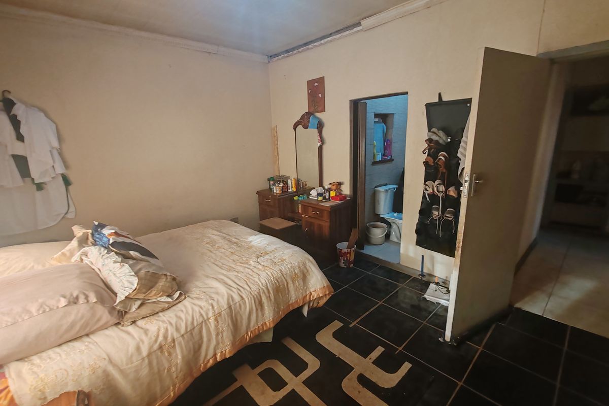 A bedroom featuring dark tiled flooring and an en-suite bathroom, requiring cosmetic updates to the walls and ceiling to improve its overall condition.