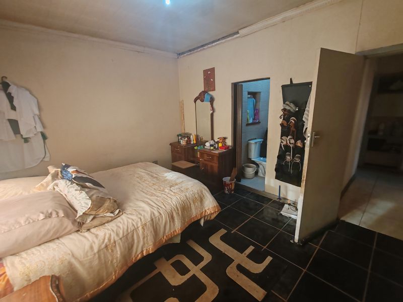 A bedroom featuring dark tiled flooring and an en-suite bathroom, requiring cosmetic updates to the walls and ceiling to improve its overall condition.