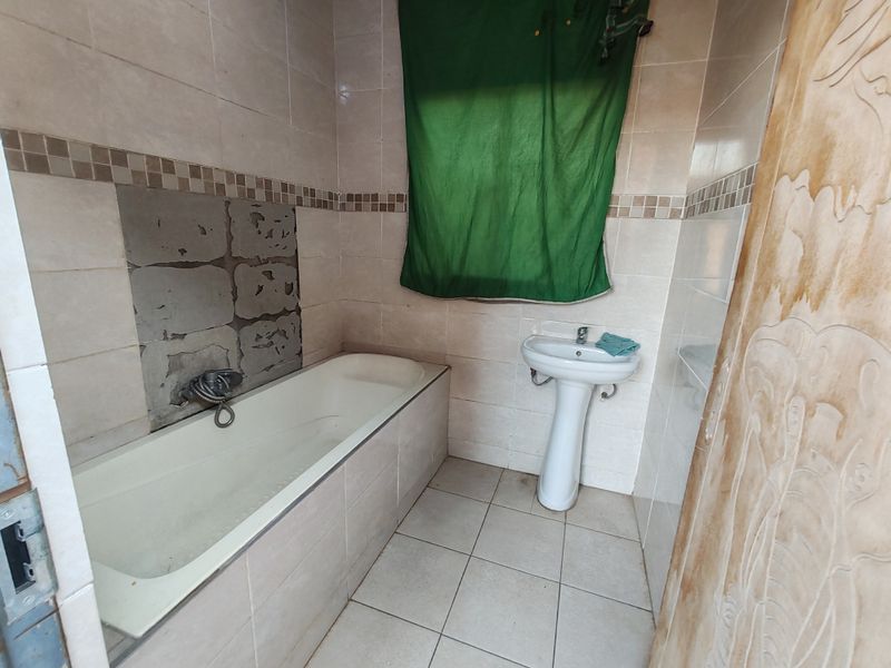 A bathroom featuring a bathtub and pedestal basin with tiled walls and flooring. The area requires maintenance to the wall finish above the bathtub.