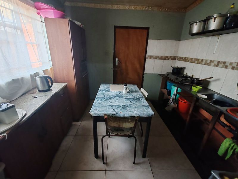 A functional kitchen featuring built-in cabinetry, a tiled backsplash, and a stainless steel sink, offering potential for modernization and aesthetic improvement.