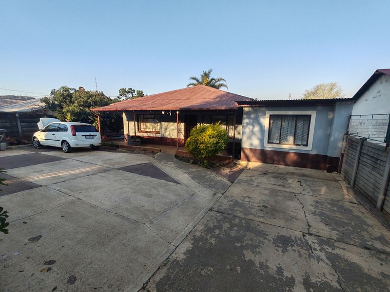 Front elevation of a single-story house featuring a corrugated metal roof, security bars on windows, and a paved concrete driveway.
