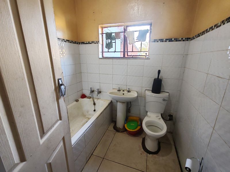 A dated bathroom featuring a standard bathtub, pedestal basin, and toilet with tiled finishes, requiring renovation to modernize the space.
