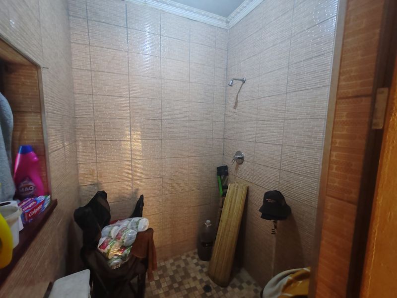 A functional bathroom shower enclosure featuring full-height wall tiling and a tiled floor, providing a basic and practical wash area.