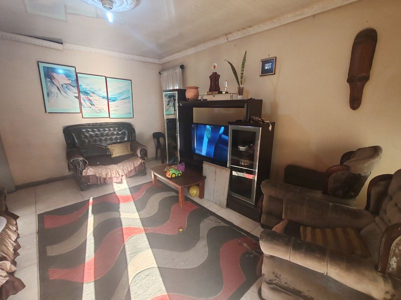 A living room featuring tiled flooring and decorative ceiling cornicing, currently showing signs of wear on the walls and ceiling requiring cosmetic attention.