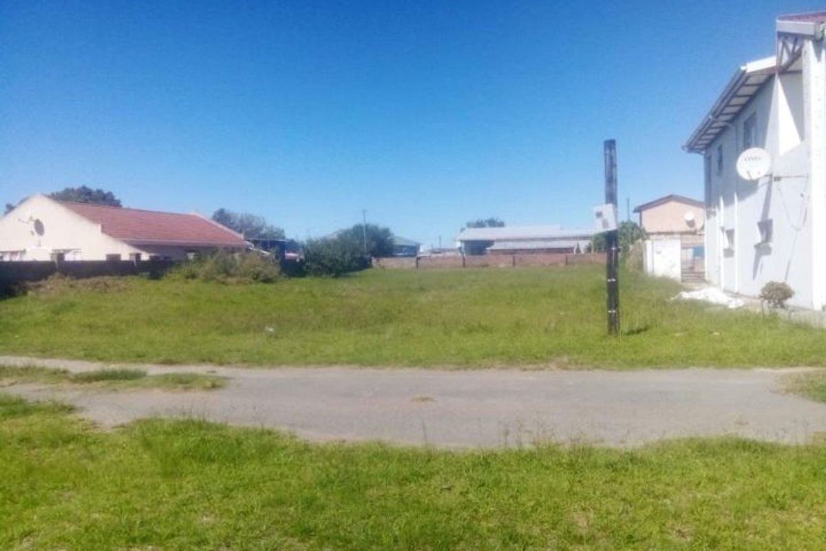 A vacant residential plot of land featuring grass coverage, a boundary wall, and an adjacent utility pole.
