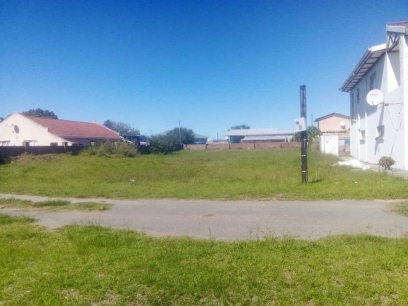 A vacant residential plot of land featuring grass coverage, a boundary wall, and an adjacent utility pole.