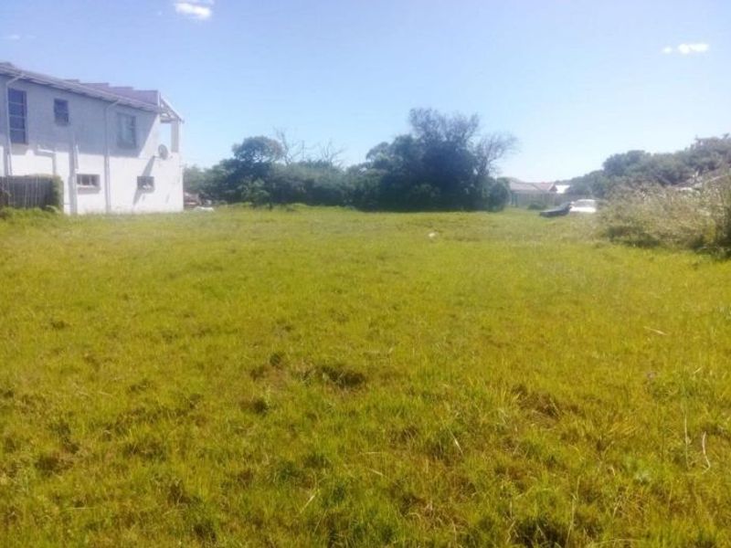 A view of a vacant residential plot featuring an open grass lawn with mature trees and adjacent building structure.