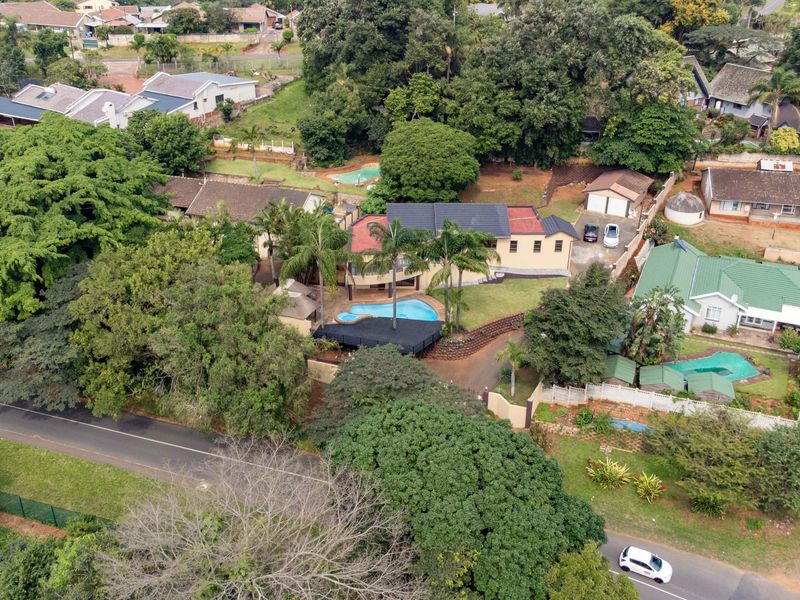 Aerial view of the property showcasing the main dwelling, swimming pool, surrounding garden, and driveway access within a residential neighborhood.