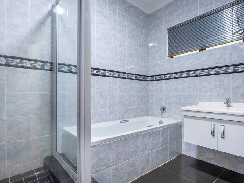 A functional bathroom featuring a built-in bathtub, separate shower enclosure, and a wall-mounted vanity unit with basin, finished with full-height wall tiling.