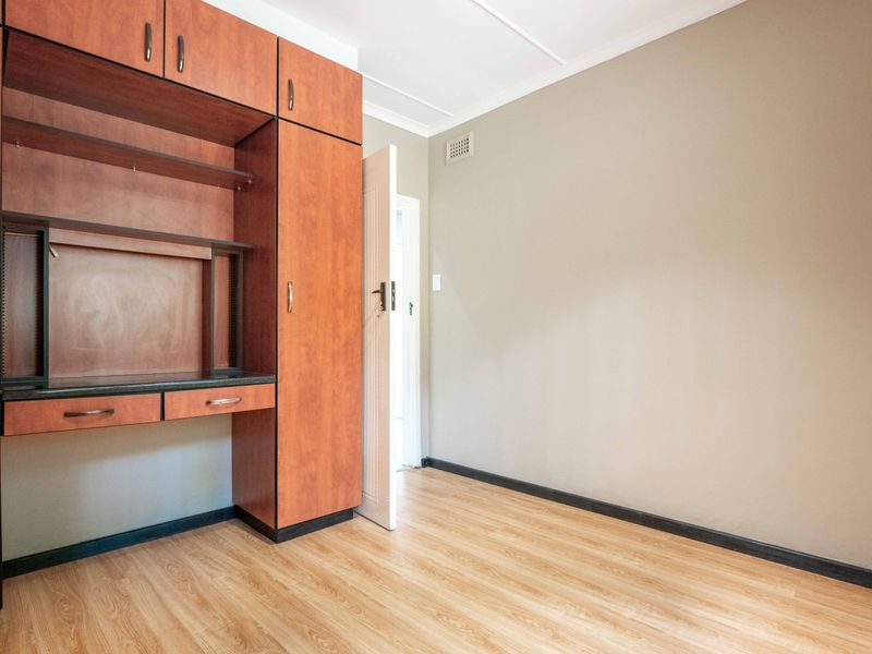 A clean, empty bedroom featuring light wood-look laminate flooring and integrated built-in cabinetry with a desk area.