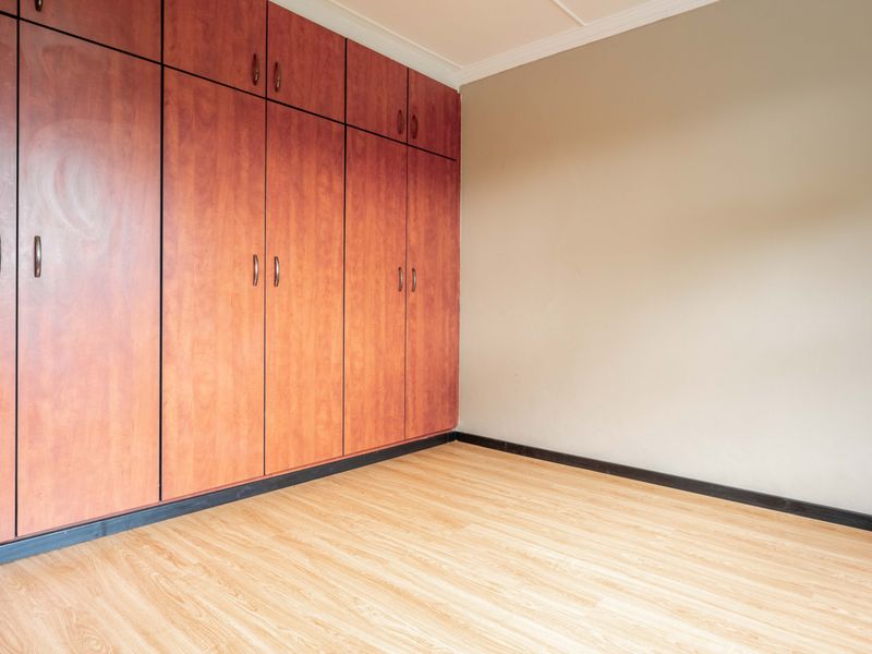 A clean, empty bedroom featuring light wood-look laminate flooring and extensive floor-to-ceiling built-in wooden cupboards.