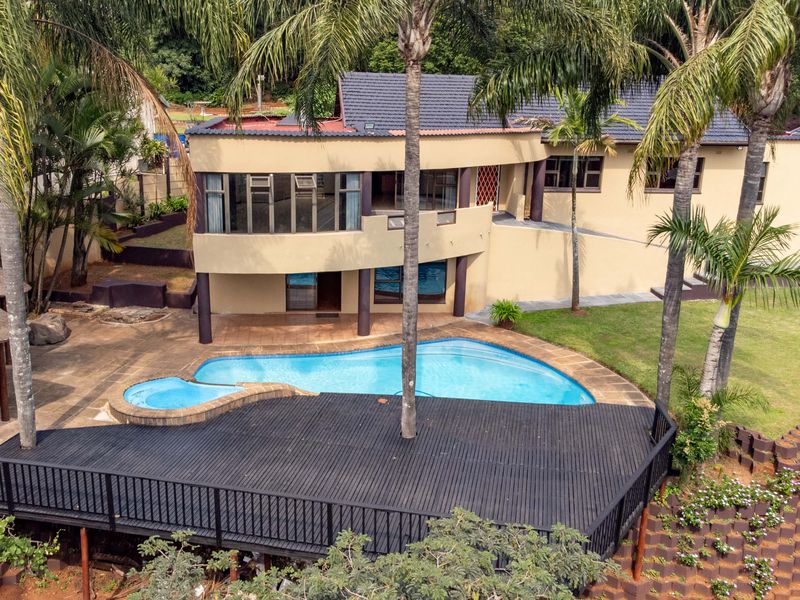 Aerial view of a multi-level residence featuring a swimming pool, a large raised timber deck, and landscaped garden areas.