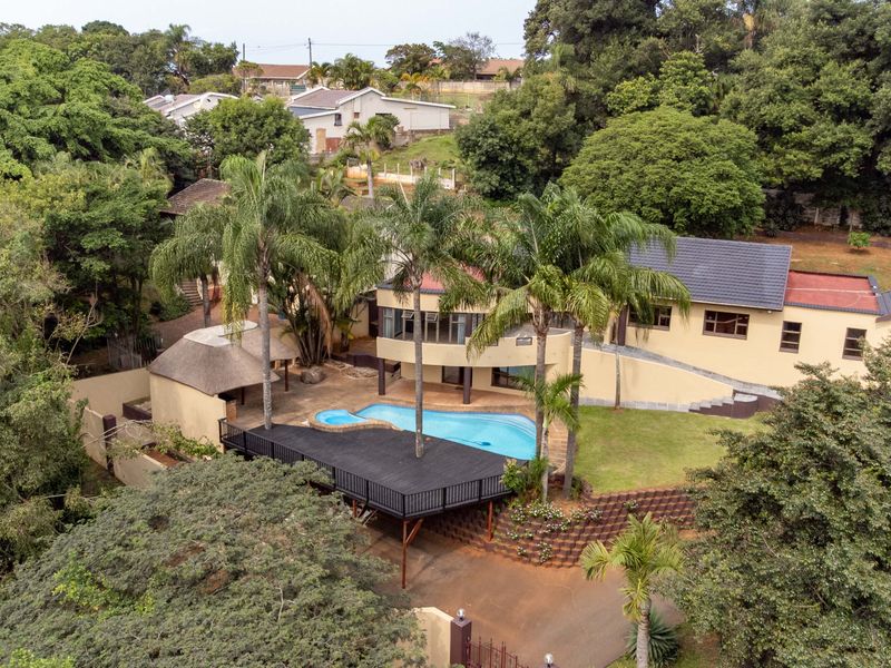 Aerial view of a residential property featuring a swimming pool, raised timber deck, thatched lapa, and landscaped garden area.