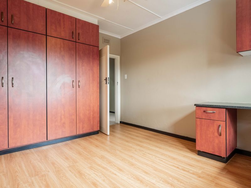 A vacant bedroom featuring laminate flooring and extensive built-in wooden cabinetry with an integrated desk area.