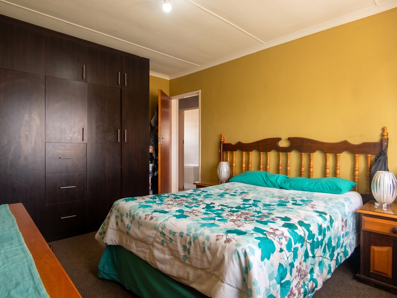 A bedroom featuring dark wood built-in cupboards and carpeted flooring, with an adjacent doorway leading to an en-suite bathroom.