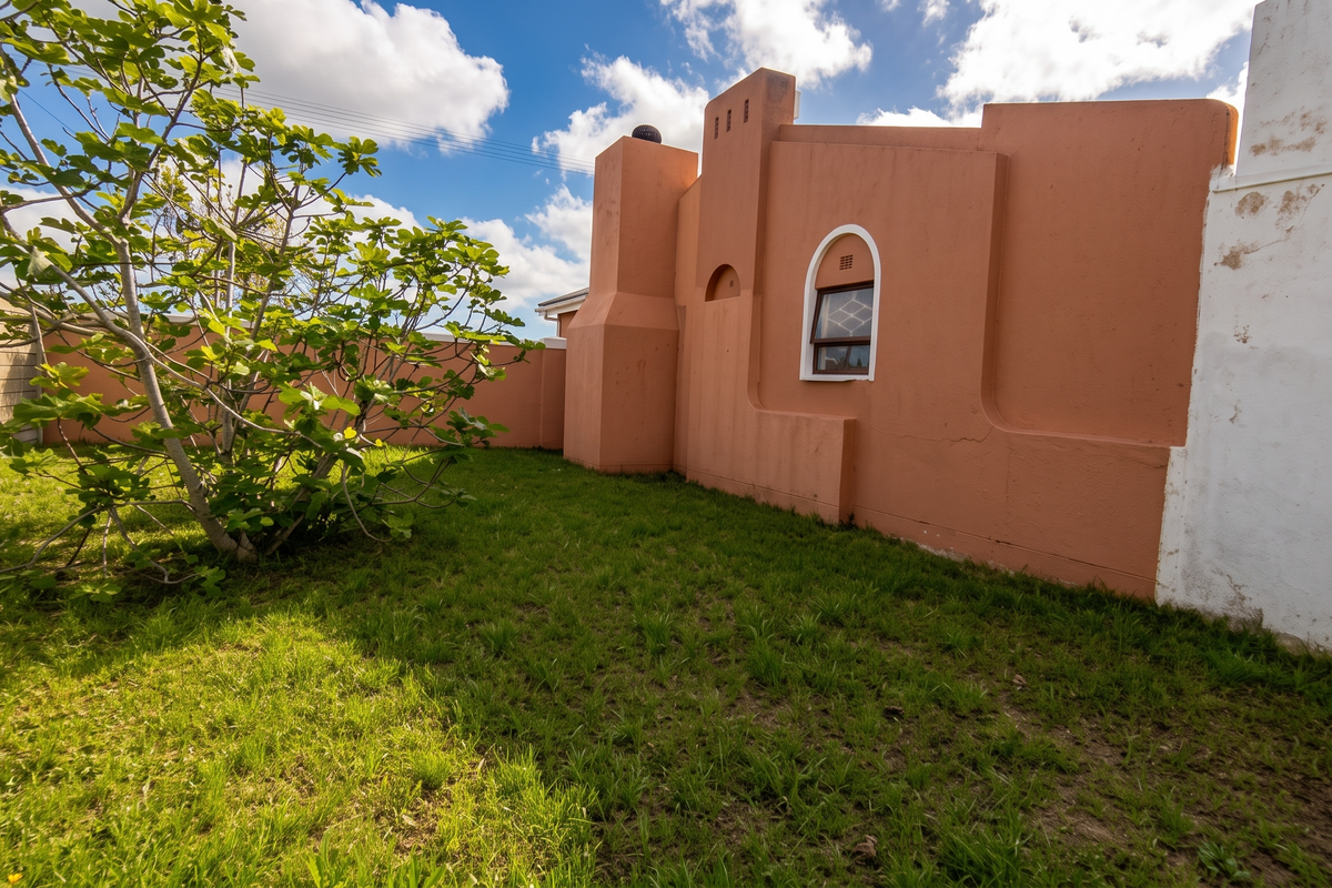 A rear garden area featuring a lawn, a mature tree, and a distinctive peach-colored exterior wall with an arched window and chimney stack.