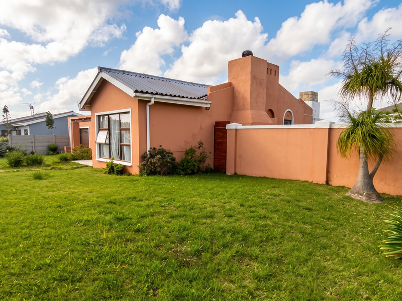 Rear view of the house featuring a peach-toned exterior, a prominent chimney, and a spacious private garden enclosed by a perimeter wall.