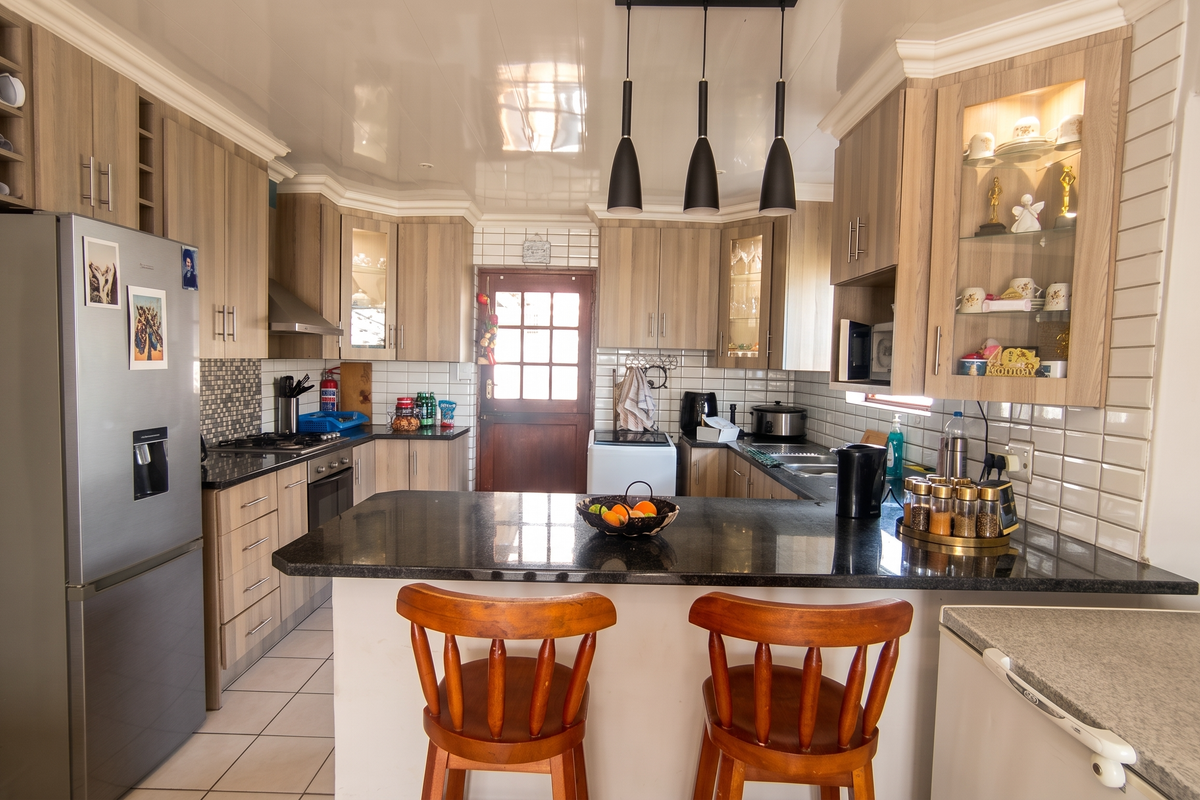 A well-appointed kitchen featuring light wood cabinetry, granite countertops, subway tile backsplash, and a central breakfast bar with pendant lighting.