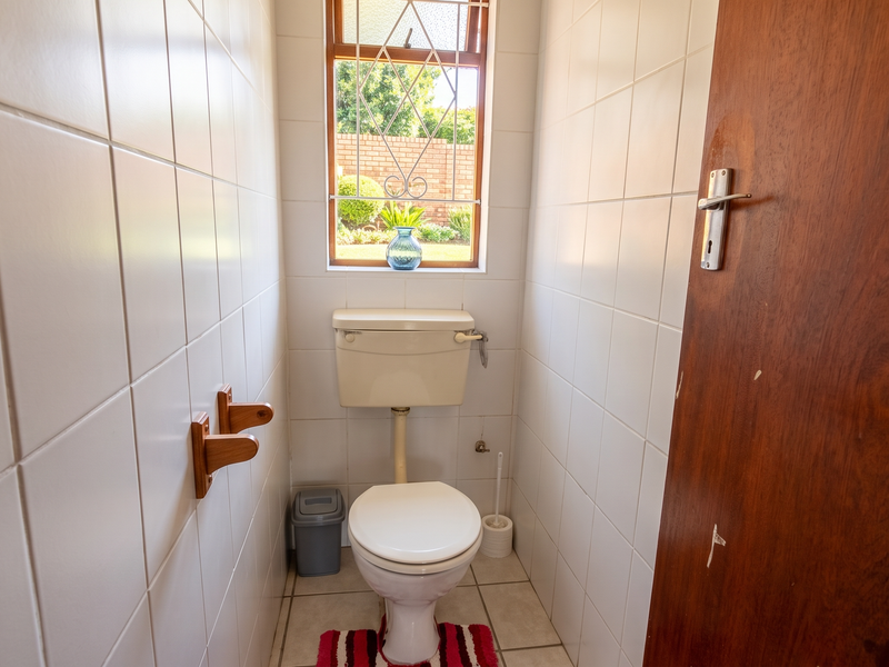 A compact guest toilet featuring full-height ceramic wall tiling, a standard toilet suite, and a timber door with security gate on the window.