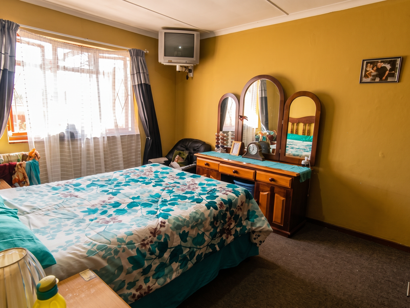 A bedroom featuring a built-in wardrobe, window with security bars, and carpeted flooring, offering a functional space with potential for cosmetic updates.