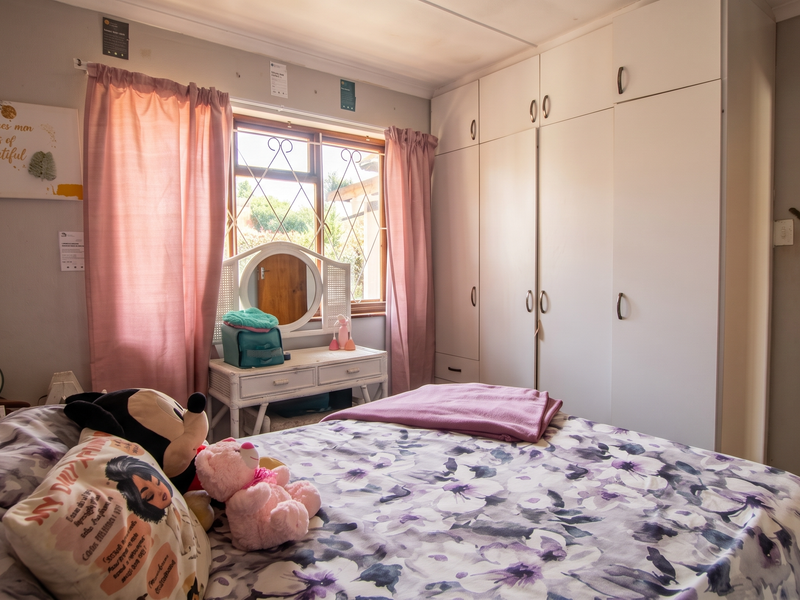 A bedroom featuring built-in cupboards and a window with security bars, providing functional storage and natural light.
