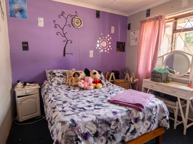 A bedroom featuring a purple accent wall, a window with security bars, and standard finishes. The room requires cosmetic updates to improve its overall appeal.