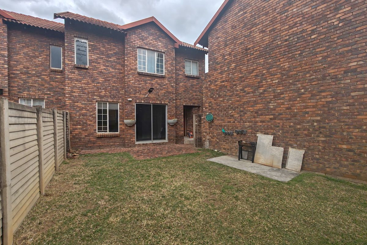 Rear view of a face brick townhouse featuring a paved patio area, small private garden, and precast concrete boundary walling.