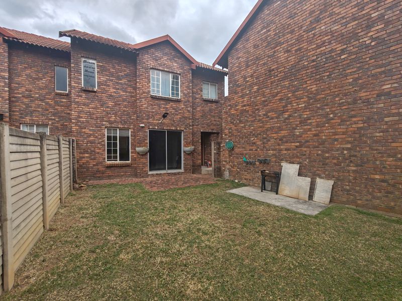 Rear view of a face brick townhouse featuring a paved patio area, small private garden, and precast concrete boundary walling.