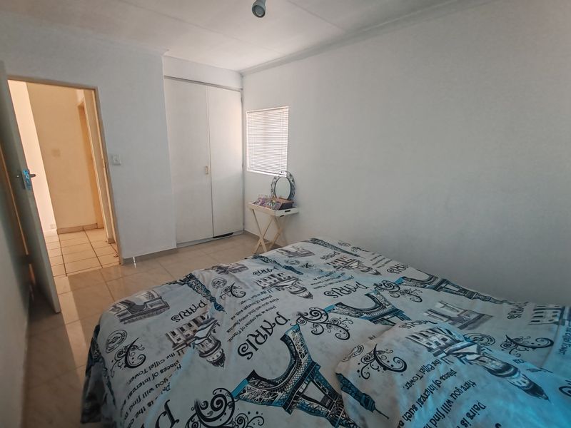 A functional bedroom featuring tiled flooring, a built-in wardrobe, and a window with a venetian blind.