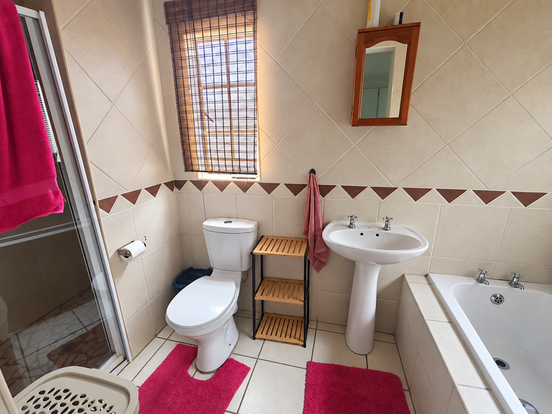 A functional bathroom featuring a pedestal basin, built-in bathtub, and a separate shower enclosure with neutral wall and floor tiling.