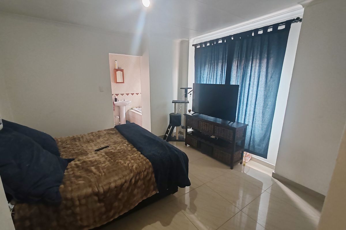 A bedroom featuring tiled flooring and direct access to an en-suite bathroom, with large windows dressed in dark curtains.