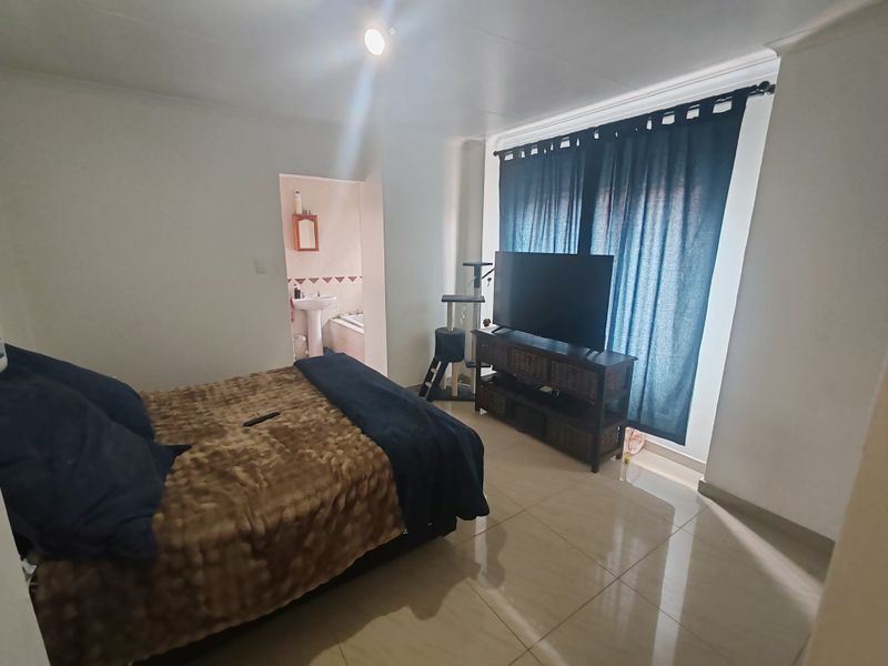 A bedroom featuring tiled flooring and direct access to an en-suite bathroom, with large windows dressed in dark curtains.