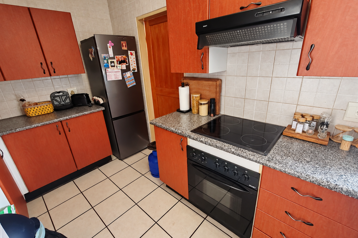 A functional kitchen featuring orange laminate cabinetry, granite-look countertops, a built-in electric oven with glass cooktop, and tiled flooring.