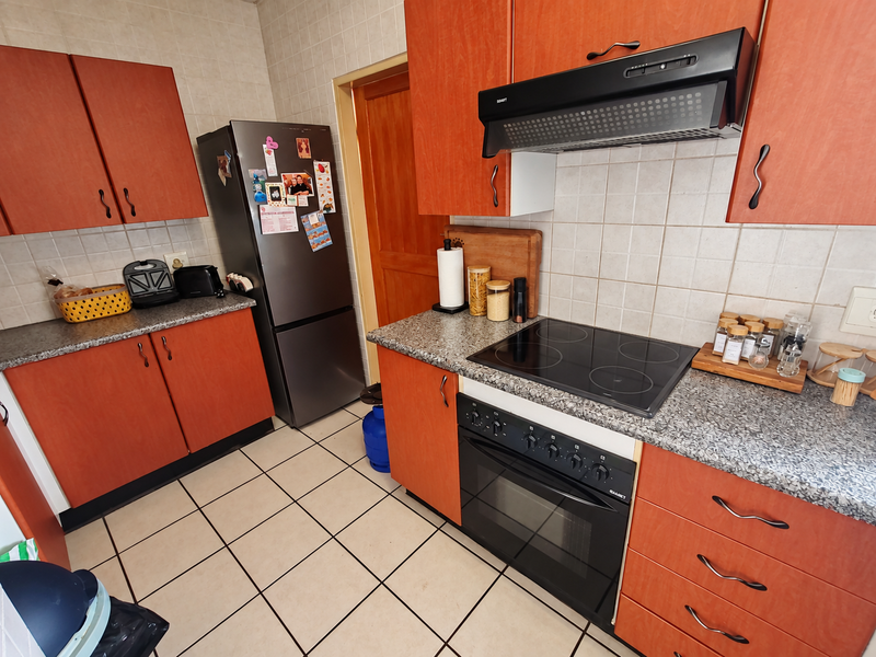A functional kitchen featuring orange laminate cabinetry, granite-look countertops, a built-in electric oven with glass cooktop, and tiled flooring.