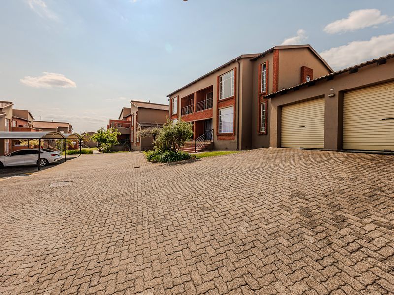 Front view of a residential apartment complex featuring a paved driveway, double garage with roller doors, and multi-story brick and plaster facade.