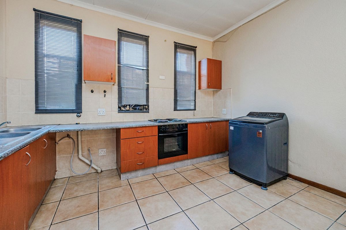 Functional kitchen featuring built-in cabinetry, laminate countertops, integrated oven and hob, tiled flooring, and tiled backsplash with exposed plumbing connections.