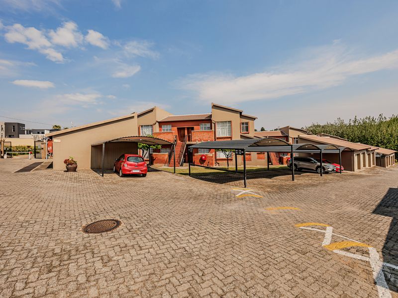 Exterior view of an apartment complex featuring a paved parking area with covered carports and brick building facades.