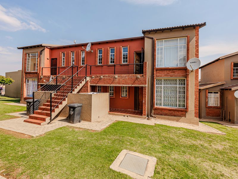 Rear view of a multi-story apartment building featuring brick construction, an external staircase, and security bars on ground-level windows.