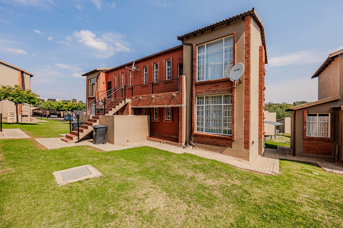 Rear view of a multi-story apartment building featuring brick facade, external metal staircase, balcony access, and surrounding landscaped lawn area.