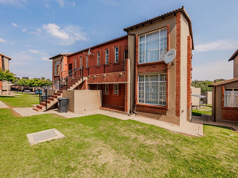 Rear view of a multi-story apartment building featuring brick facade, external metal staircase, balcony access, and surrounding landscaped lawn area.