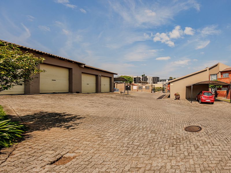 Exterior view of the apartment complex featuring a paved driveway, multiple garage units, and a covered carport area.
