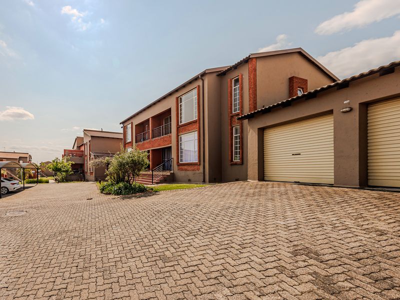 Exterior view of a multi-story apartment complex featuring a paved driveway, integrated garages, and brick-accented facade.