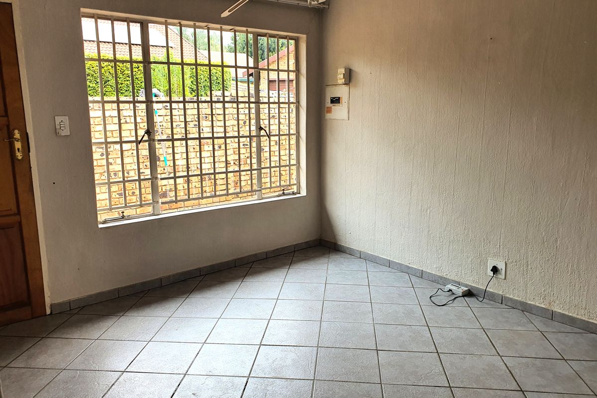 An empty living room featuring tiled flooring, security bars on the window, and an exposed electrical distribution board on the wall.