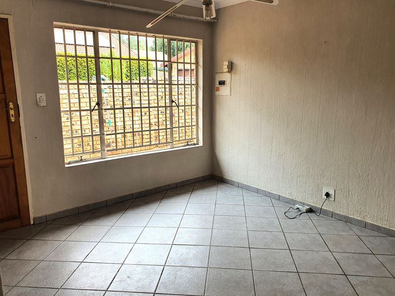An empty living room featuring tiled flooring, security bars on the window, and an exposed electrical distribution board on the wall.