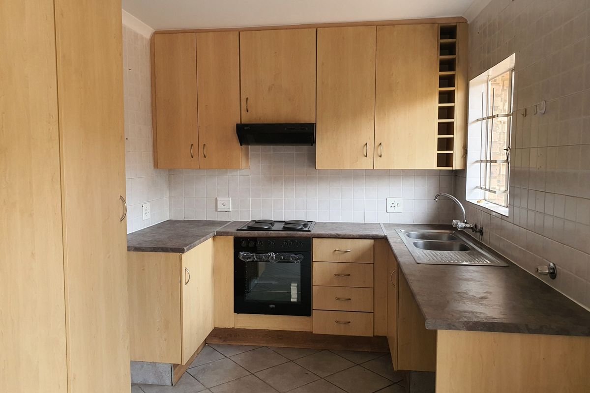 A functional kitchen featuring light wood-finish cabinetry, laminate countertops, a built-in oven with hob, and a stainless steel sink with tiled backsplash.