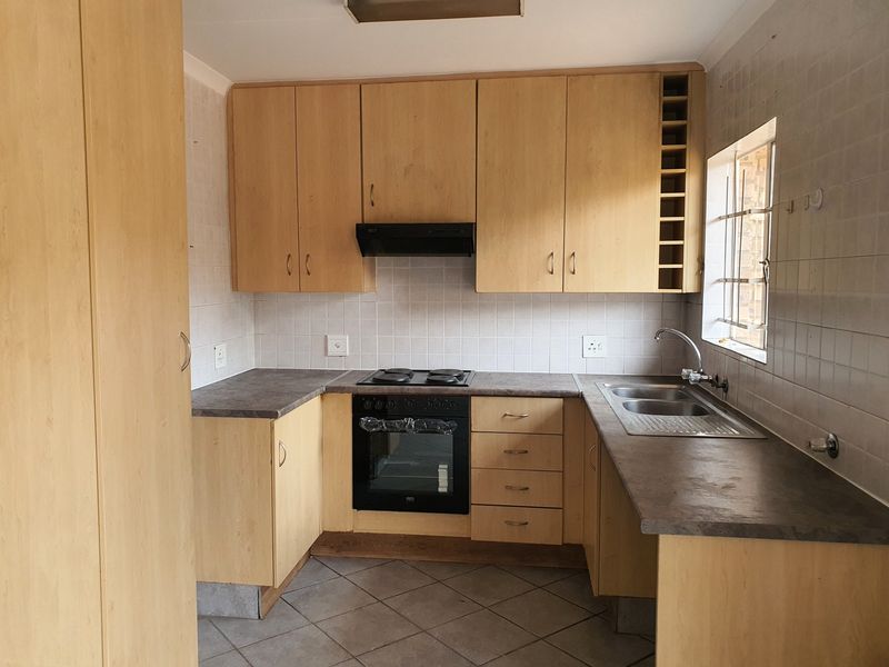 A functional kitchen featuring light wood-finish cabinetry, laminate countertops, a built-in oven with hob, and a stainless steel sink with tiled backsplash.